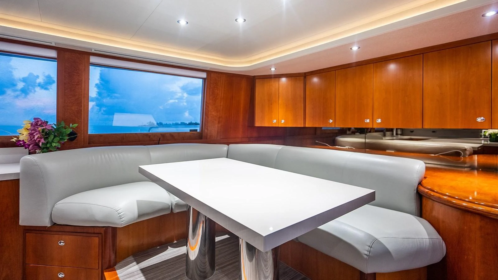 The yacht's dining area features a sleek, modern table surrounded by comfortable seating and warm wood cabinetry. aboard KEMOSABE Yacht for Sale