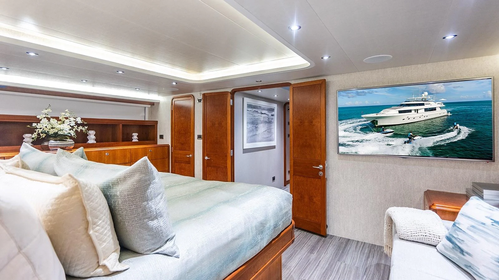 A luxurious stateroom featuring a large bed, elegant wood finishes, and a flat-screen TV displaying a yacht. aboard KEMOSABE Yacht for Sale