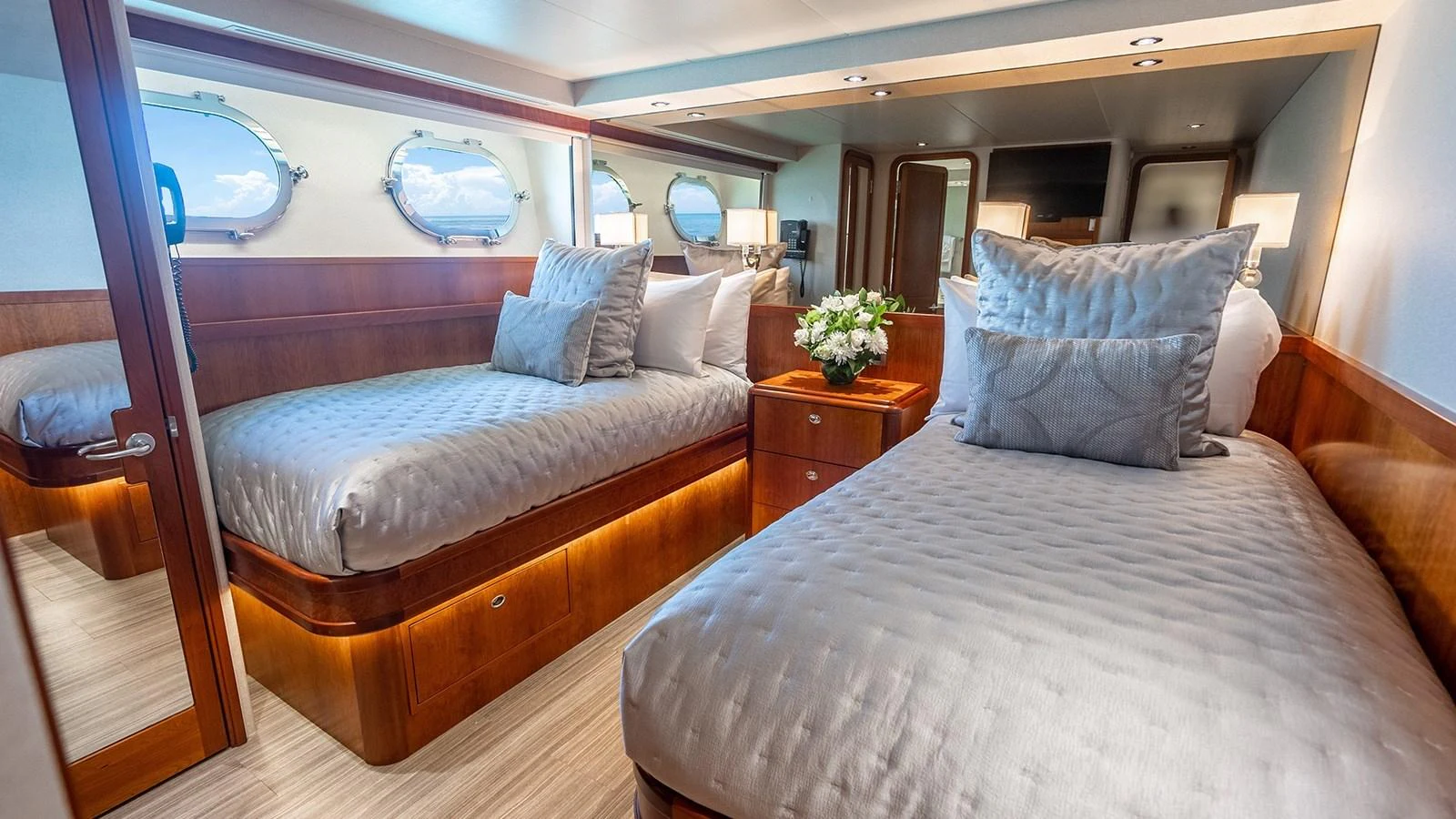 The guest stateroom features twin beds, elegant wood finishes, and ample natural light from the portholes. aboard KEMOSABE Yacht for Sale