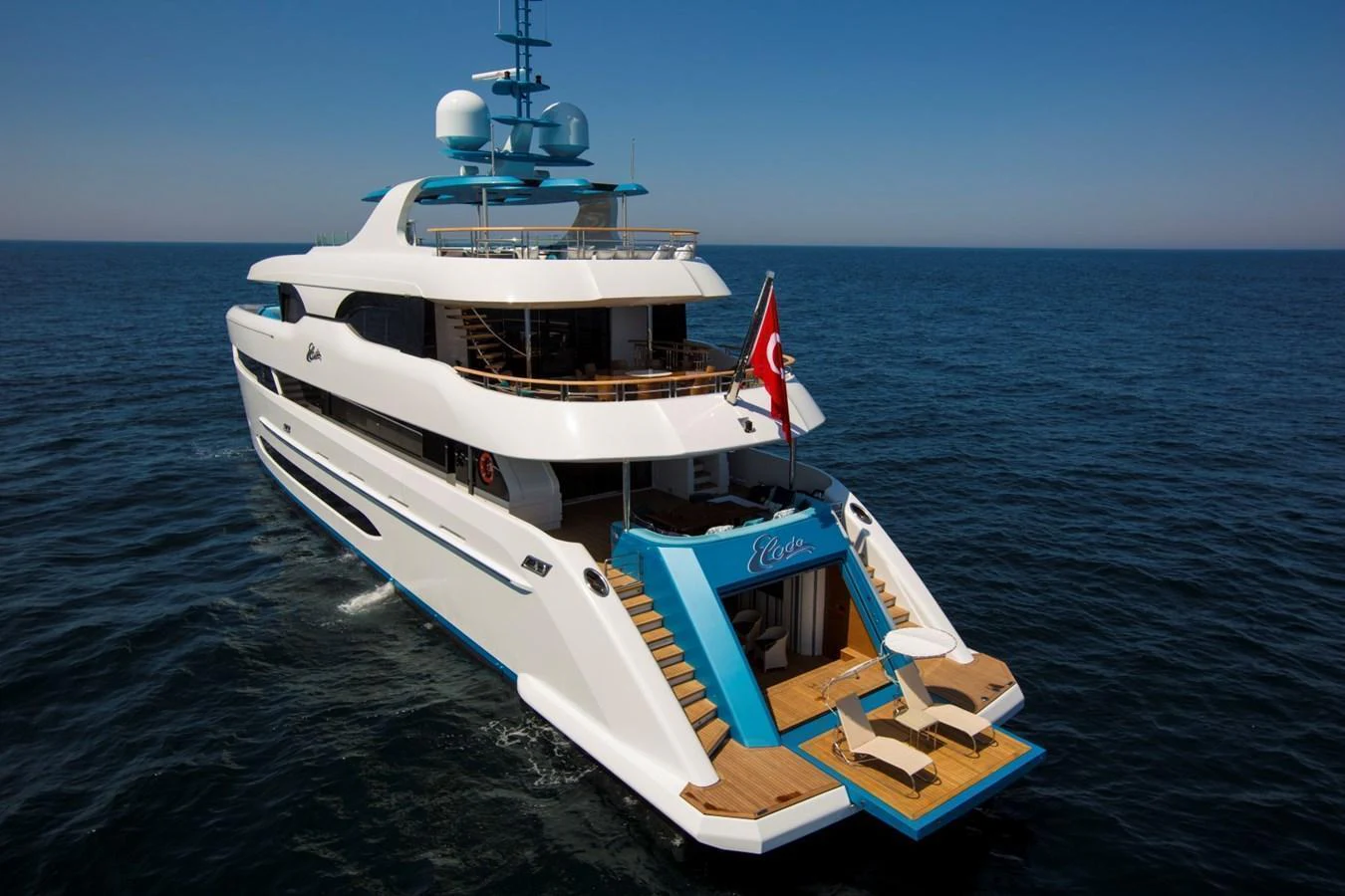 A luxurious yacht cruising on the open sea with an inviting aft deck featuring a seating area and steps leading to the water. aboard ELADA Yacht for Sale