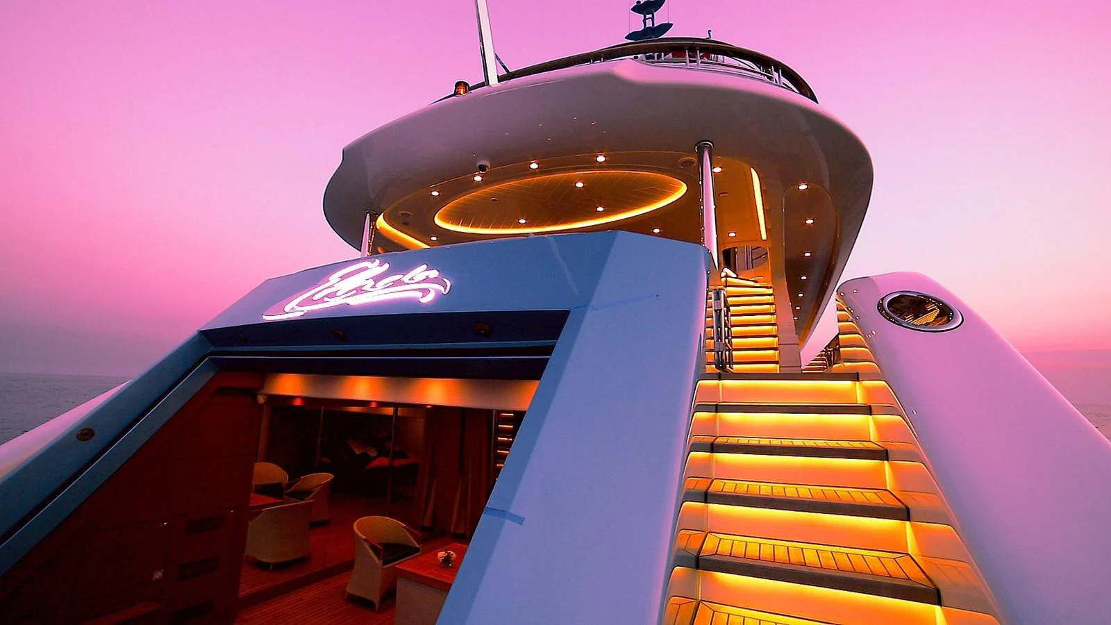 The yacht's aft deck is illuminated with warm lighting, creating an inviting ambiance against a stunning sunset backdrop. aboard ELADA Yacht for Sale