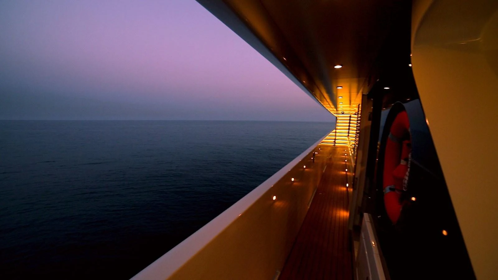 A serene view of the yacht's side deck at twilight, showcasing elegant lighting and a calm sea. aboard ELADA Yacht for Sale