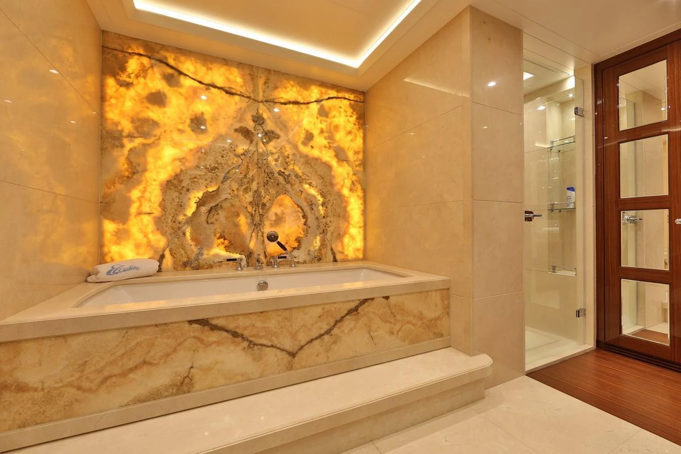 The luxurious bathroom features a stunning backlit onyx wall and a spacious bathtub. aboard ELADA Yacht for Sale