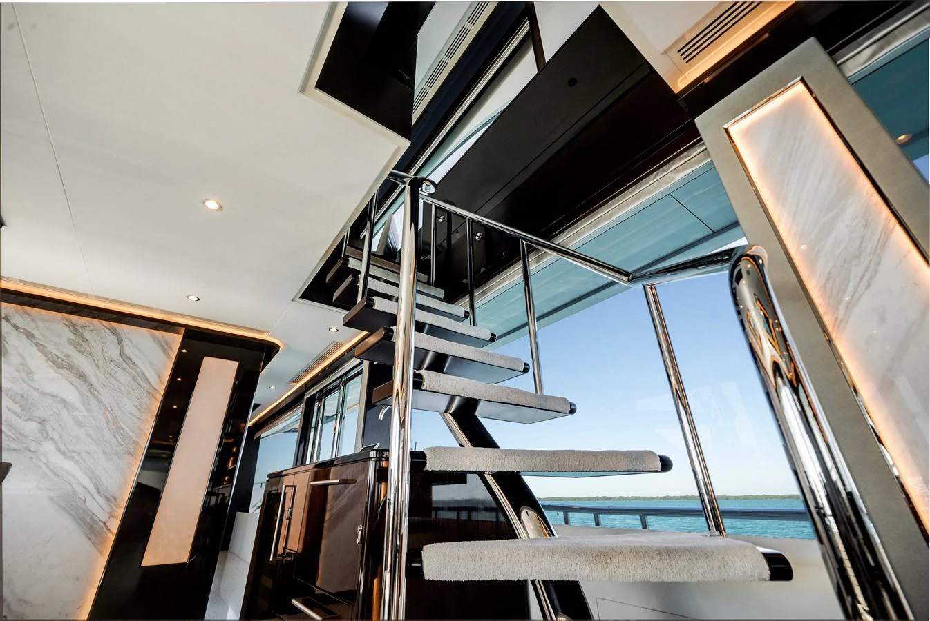 A modern yacht interior featuring a sleek staircase with a view of the ocean through large windows. aboard OCEAN ALEXANDER 37L/01 Yacht for Sale