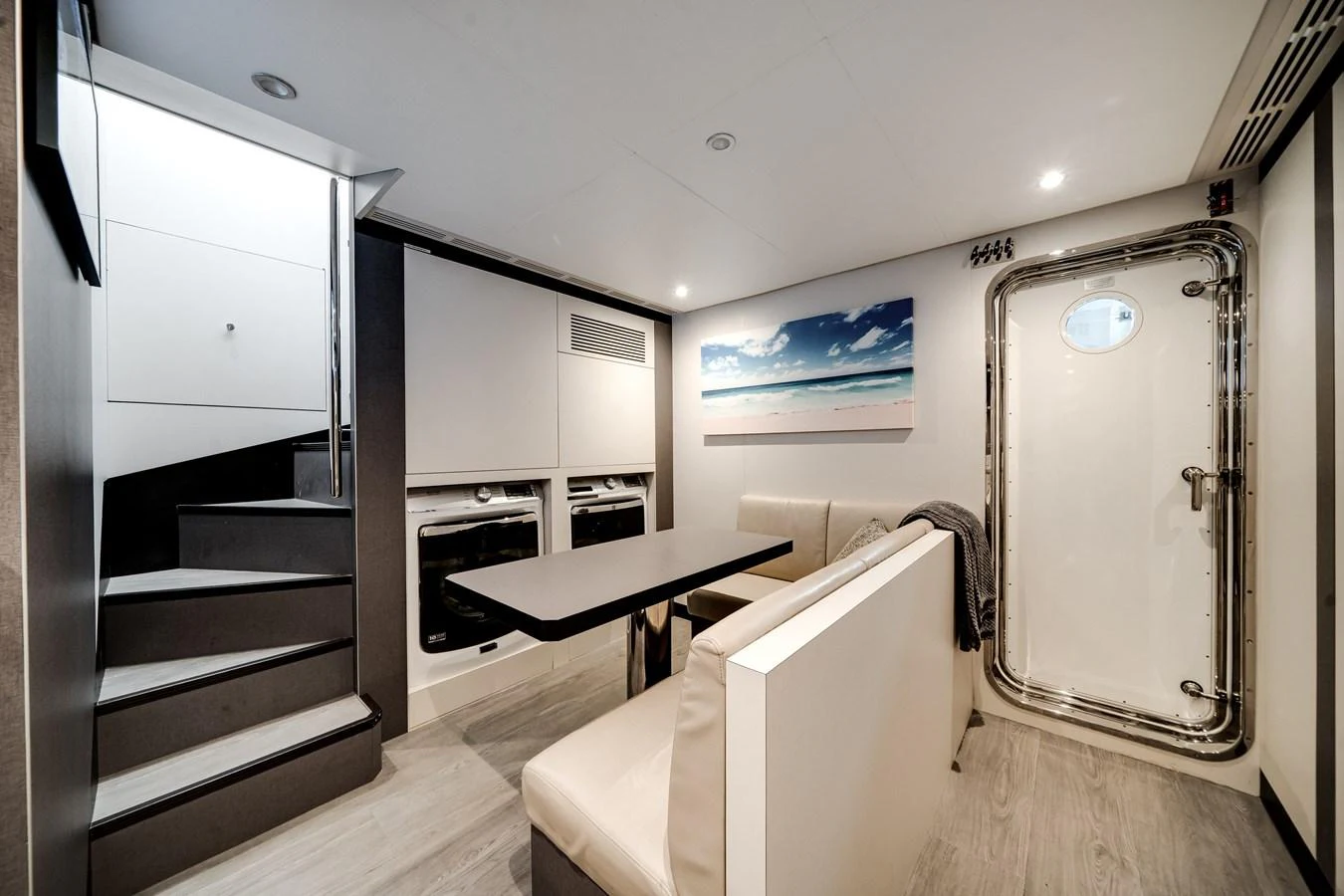 The yacht's interior features a cozy dining area with a modern table and comfortable seating, complemented by a beach-themed artwork and a polished metal door. aboard OCEAN ALEXANDER 37L/01 Yacht for Sale