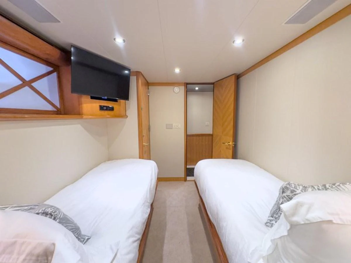 The twin stateroom features two single beds, a wall-mounted TV, and elegant wood accents. aboard BREAKAWAY Yacht for Sale