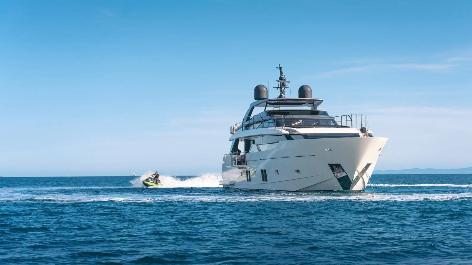 A sleek yacht cruising on open water with a jet ski riding alongside. aboard JOURNEY Yacht for Sale