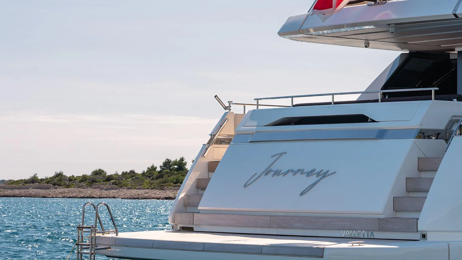 The yacht's aft deck features elegant design elements and a serene backdrop of calm waters and distant shoreline. aboard JOURNEY Yacht for Sale