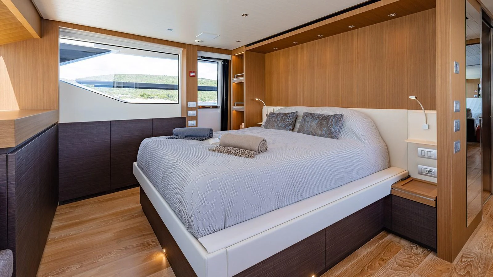 The master stateroom features a spacious bed with modern wooden accents and ample natural light. aboard JOURNEY Yacht for Sale