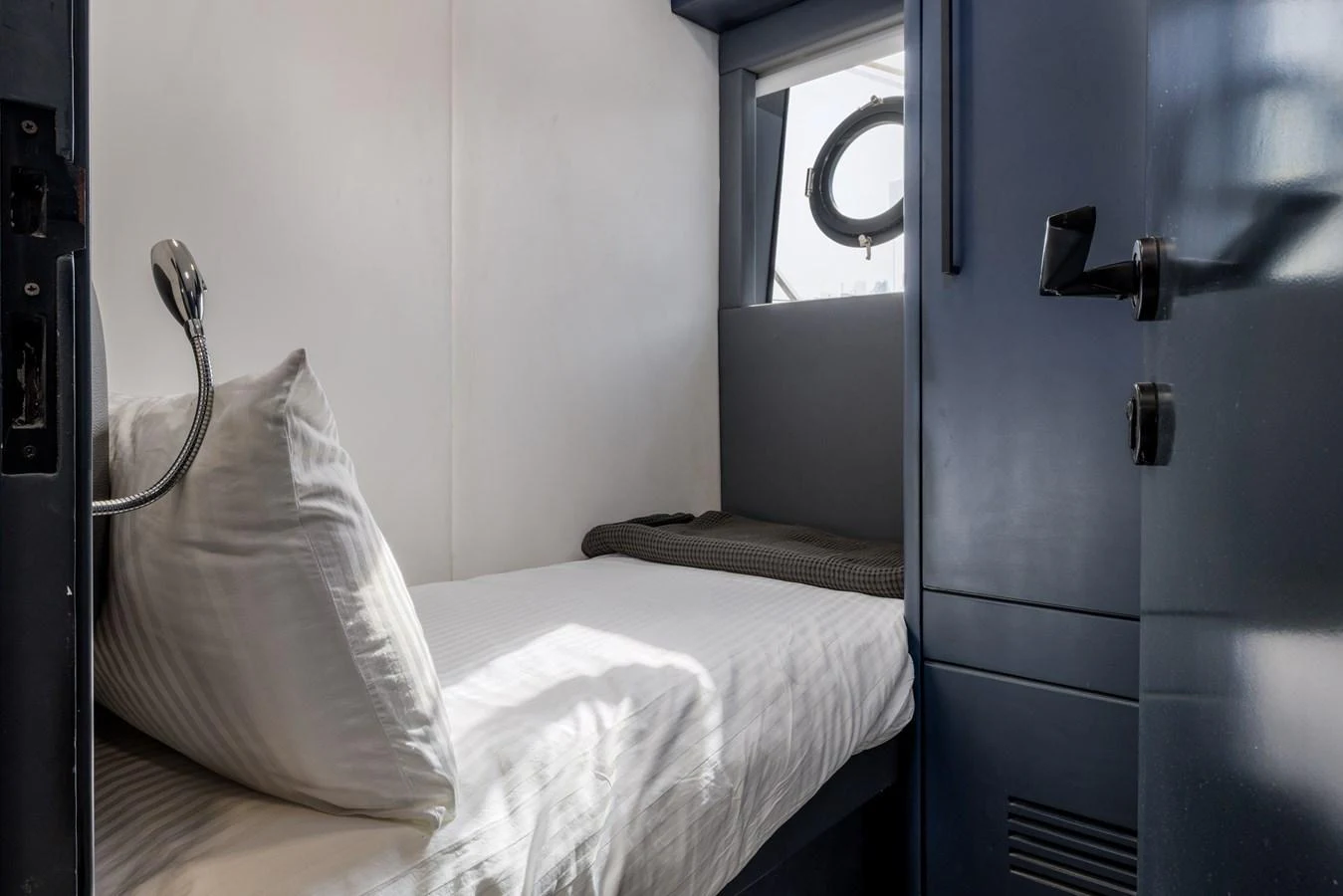 A cozy cabin with a single bed and a porthole window providing natural light. aboard AL SULTAN Yacht for Sale