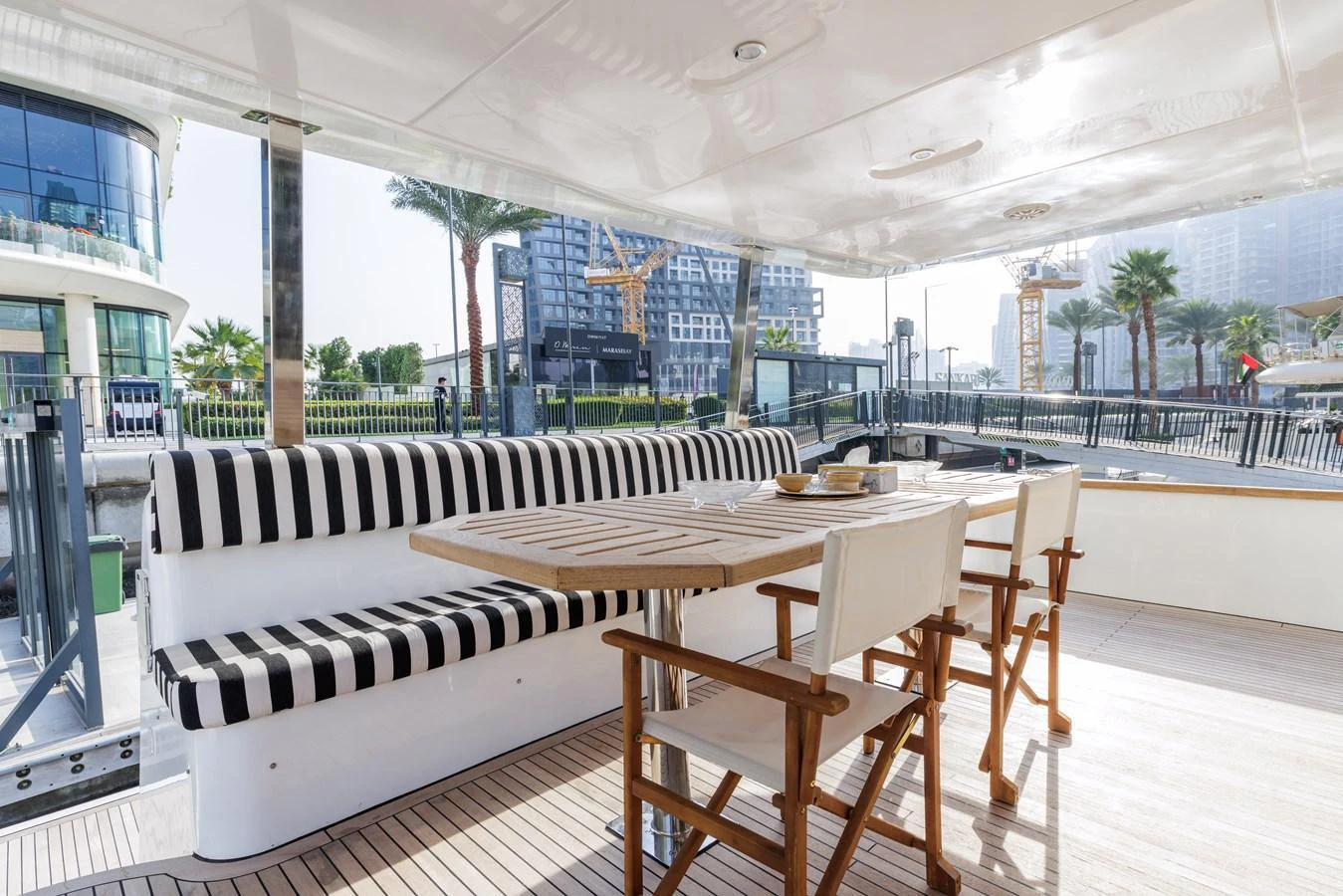The aft deck features a stylish dining area with striped seating and wooden chairs, perfect for alfresco meals. aboard AL SULTAN Yacht for Sale