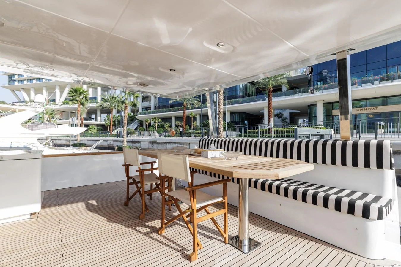 The aft deck features a stylish dining area with a striped cushioned bench and wooden table, perfect for alfresco meals. aboard AL SULTAN Yacht for Sale