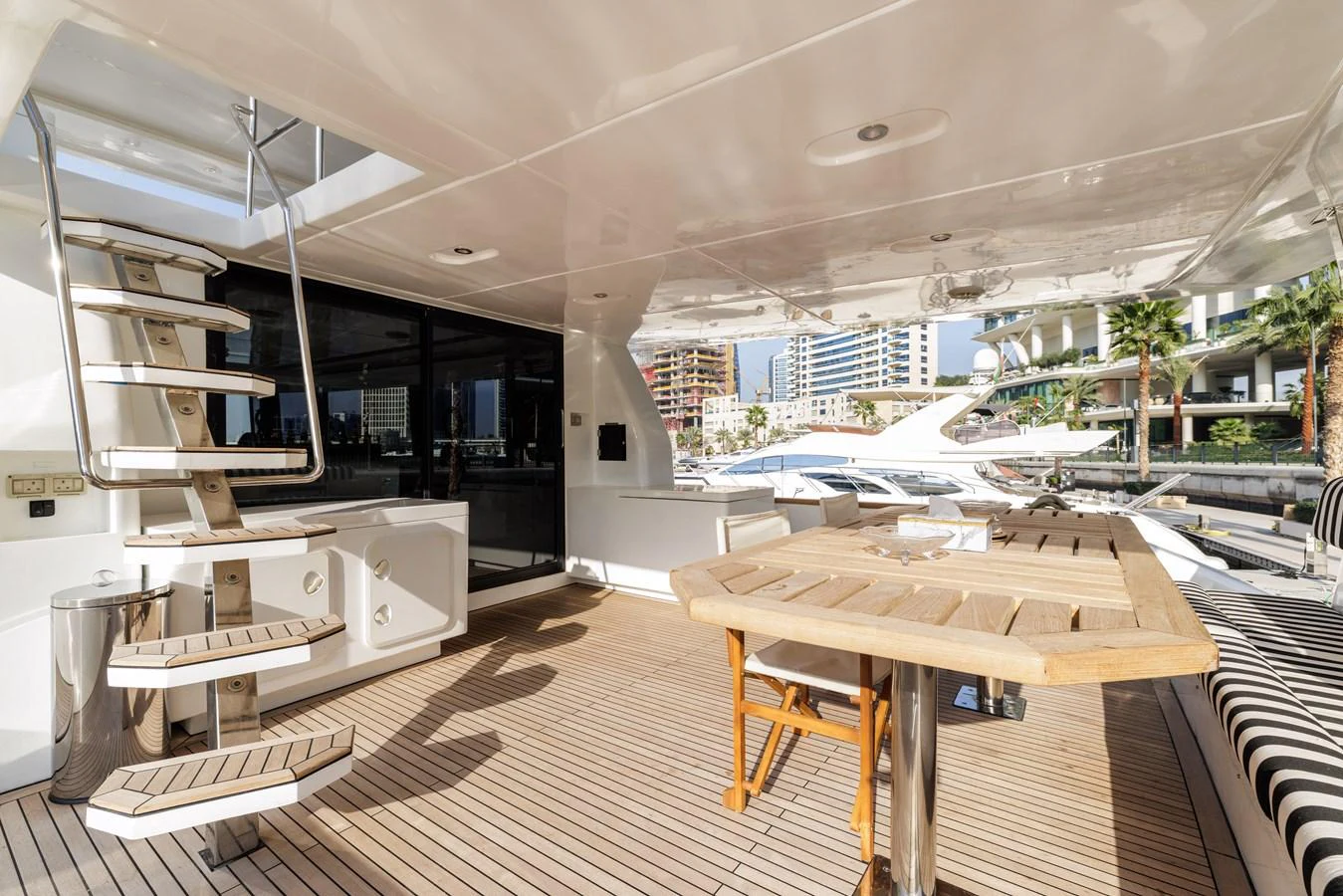 The aft deck features a spacious seating area with a wooden table and modern staircase. aboard AL SULTAN Yacht for Sale