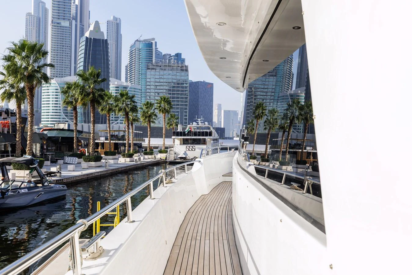 The yacht's side deck offers a sleek walkway with a stunning cityscape backdrop. aboard AL SULTAN Yacht for Sale