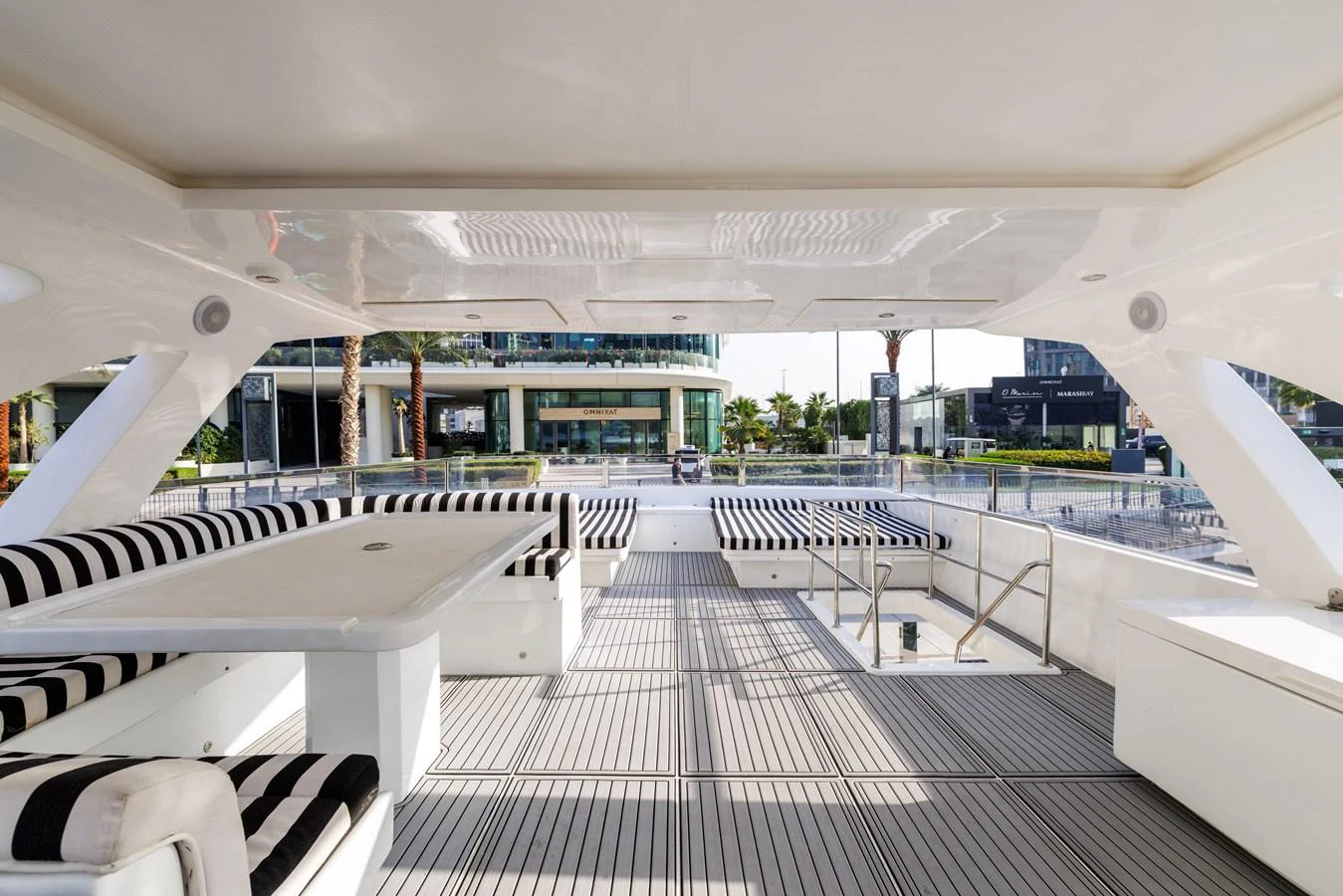 The aft deck features a spacious seating area with striped cushions and a large table, perfect for outdoor dining and relaxation. aboard AL SULTAN Yacht for Sale