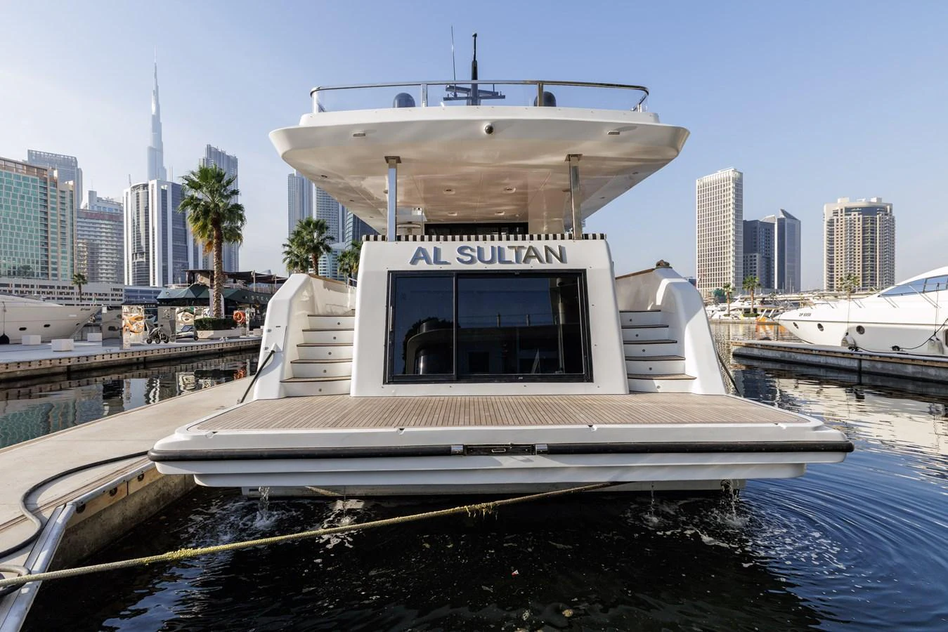 The yacht is docked in a marina, showcasing its spacious aft deck with steps leading up to the main deck. aboard AL SULTAN Yacht for Sale