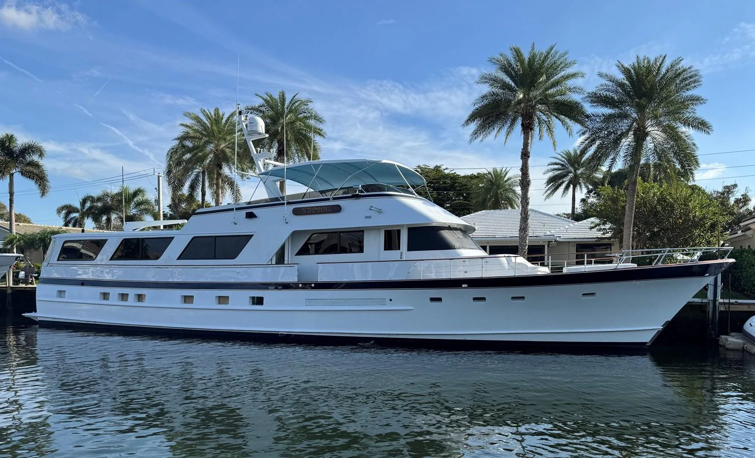 A classic motor yacht is docked in a serene marina, surrounded by palm trees and clear blue skies. aboard SHEPSL X Yacht for Sale