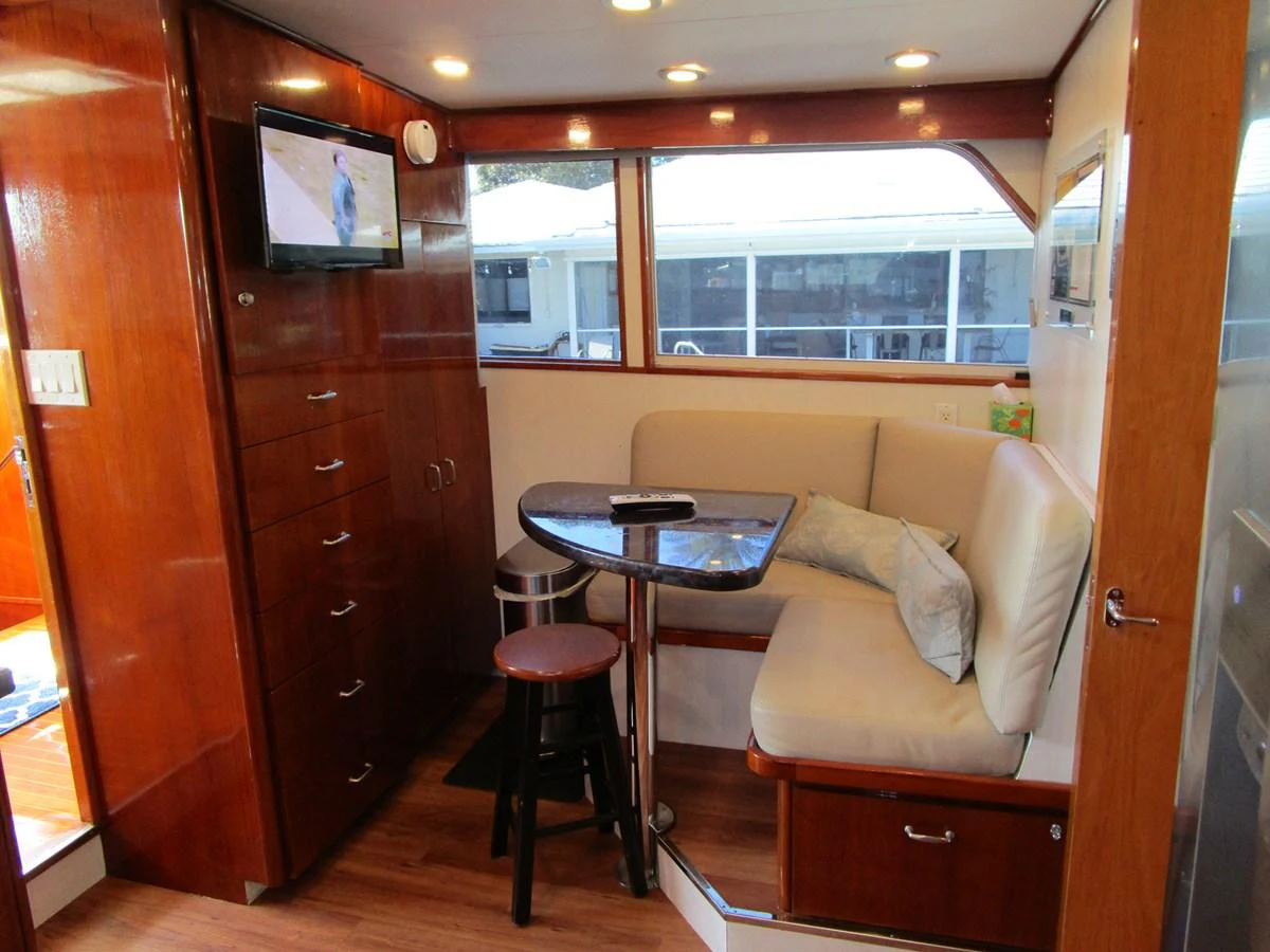 The cozy salon features a comfortable seating area with a small dining table and a mounted television. aboard SHEPSL X Yacht for Sale