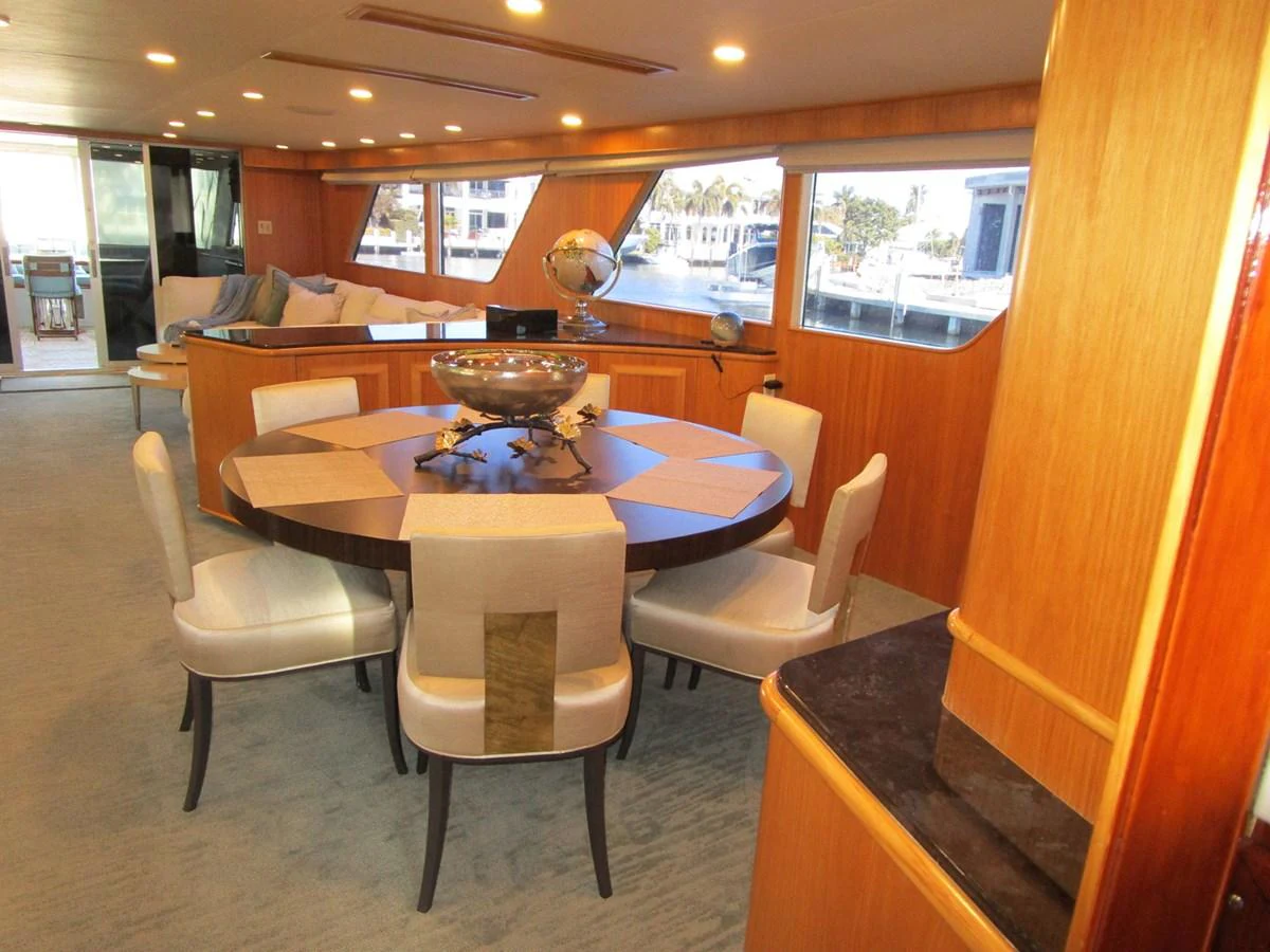 The yacht's dining area features a stylish round table with elegant seating, set against large windows offering scenic views. aboard SHEPSL X Yacht for Sale