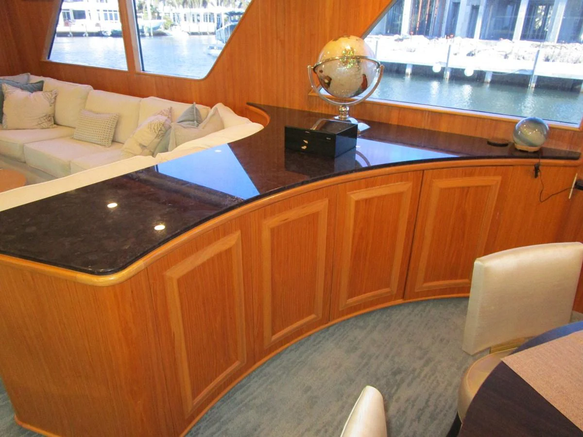 The yacht's interior features a stylish seating area with a curved wooden counter and large windows offering a view of the marina. aboard SHEPSL X Yacht for Sale