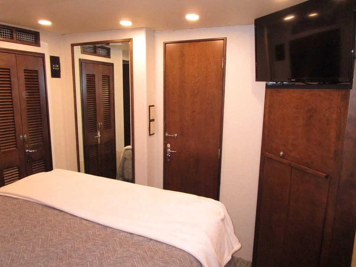 A cozy stateroom featuring a comfortable bed, wooden cabinetry, and a mounted TV. aboard SHEPSL X Yacht for Sale