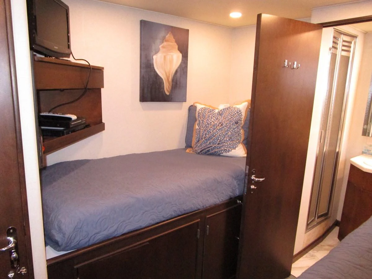 A cozy guest cabin featuring a single bed with blue bedding and a small entertainment setup. aboard SHEPSL X Yacht for Sale
