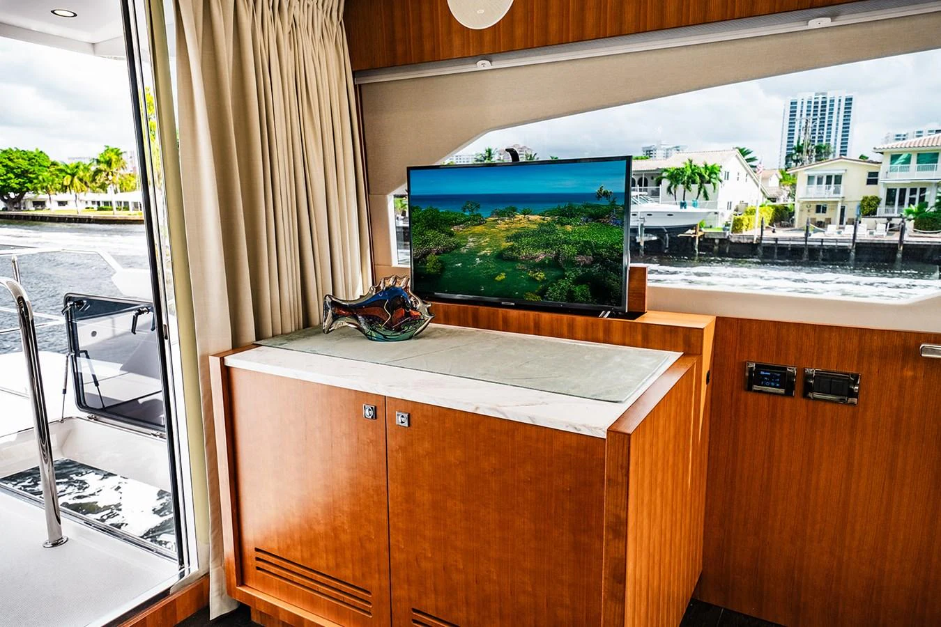 The interior features a sleek entertainment area with a large window offering a view of the water and cityscape. aboard INDIGO Yacht for Sale