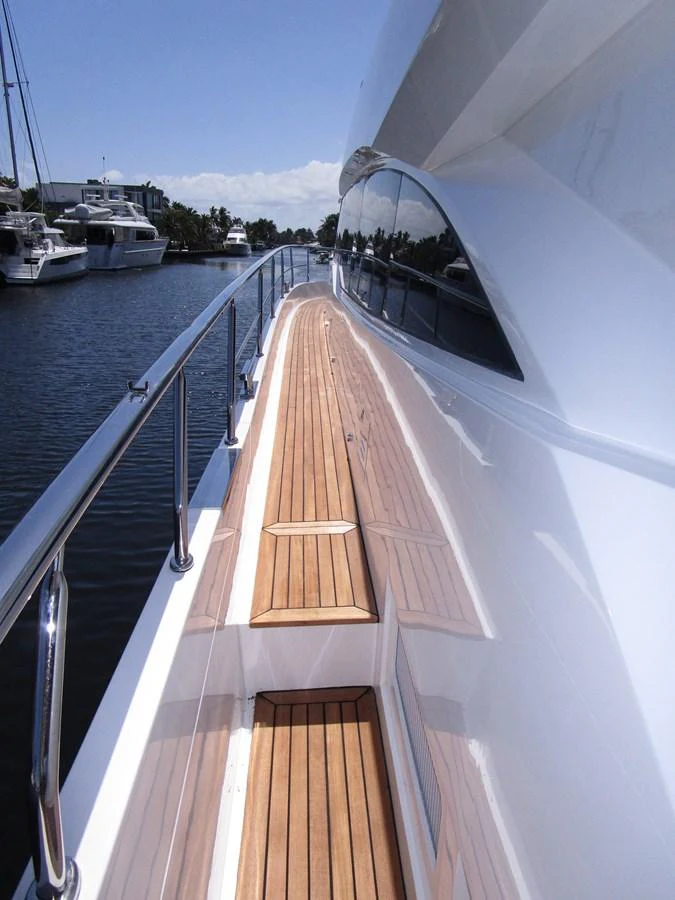 The image showcases the sleek and polished side deck of a yacht, featuring a wooden walkway and stainless steel railings. aboard INDIGO Yacht for Sale