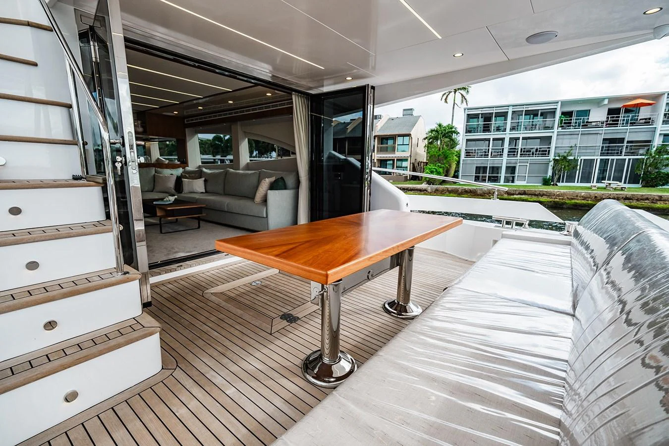 The aft deck features a sleek wooden table and comfortable seating, seamlessly connecting to the luxurious interior salon. aboard INDIGO Yacht for Sale