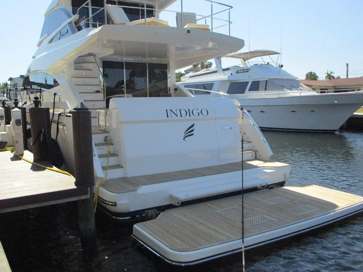 The yacht is docked at a marina, showcasing its spacious aft deck and swim platform. aboard INDIGO Yacht for Sale