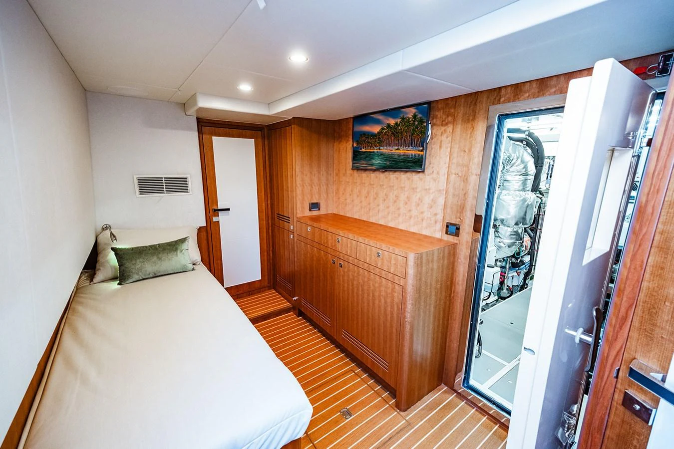 A cozy crew cabin with a single bed, wooden cabinetry, and access to the engine room. aboard INDIGO Yacht for Sale