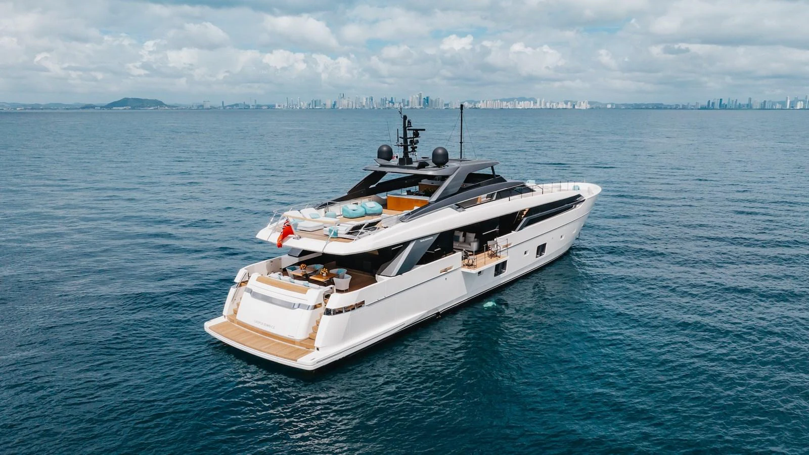 A sleek and modern yacht cruises gracefully on calm waters with a cityscape in the background. aboard AMBAR Yacht for Sale