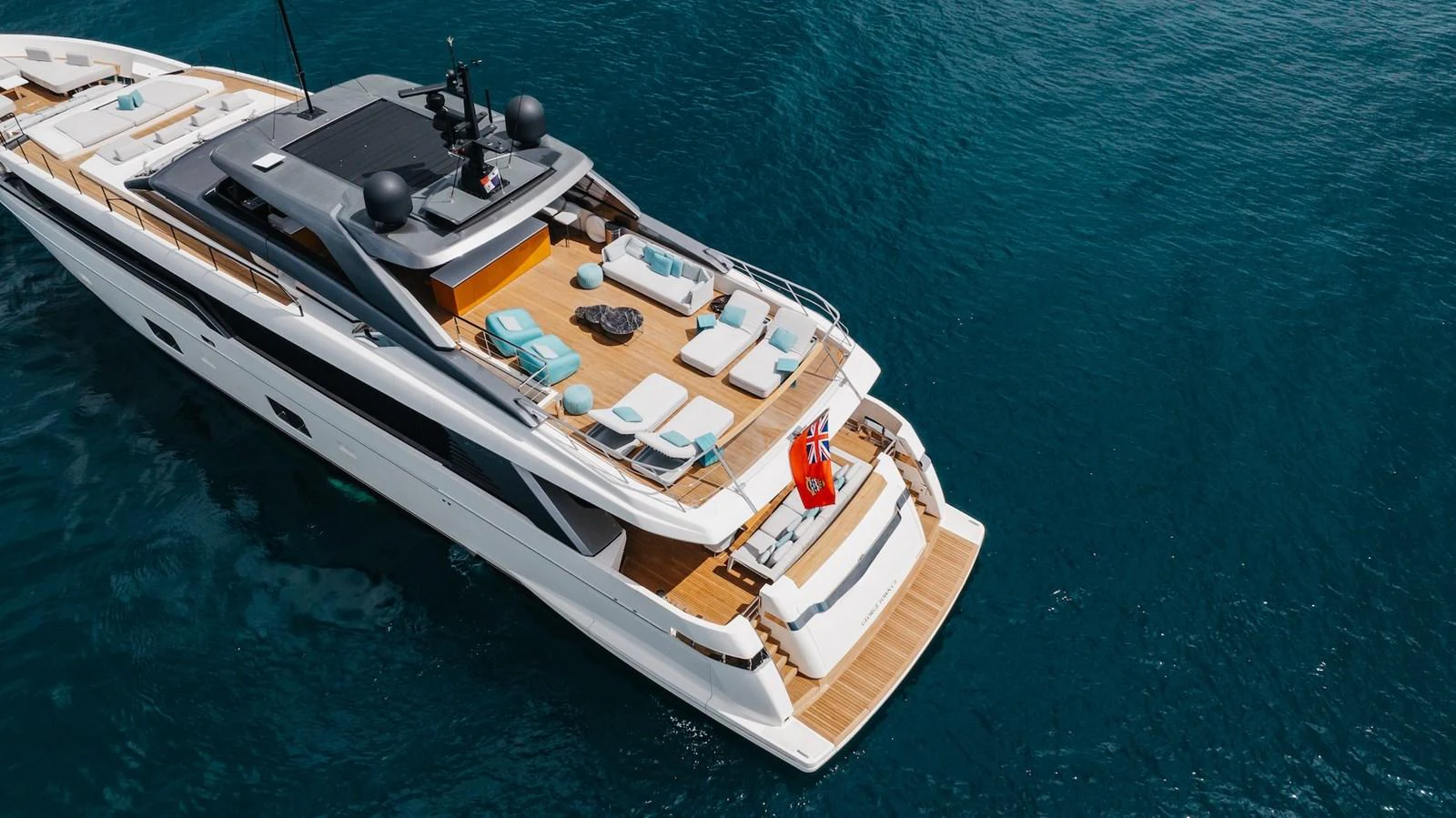 A luxurious yacht with a spacious aft deck featuring sun loungers and a swim platform, cruising on clear blue waters. aboard AMBAR Yacht for Sale