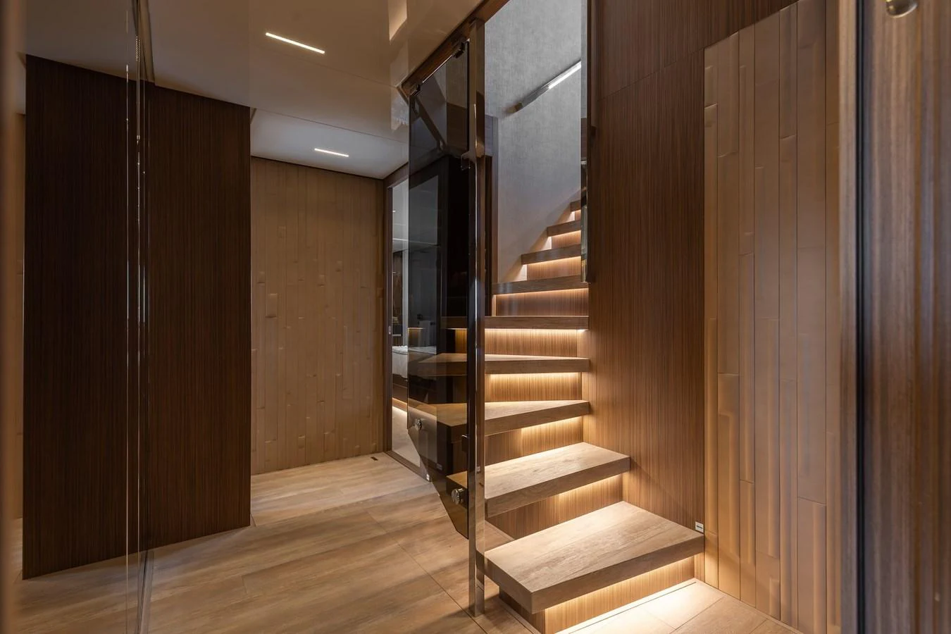 The image showcases a modern and elegant staircase within the yacht's interior, featuring warm wooden tones and ambient lighting. aboard AMBAR Yacht for Sale