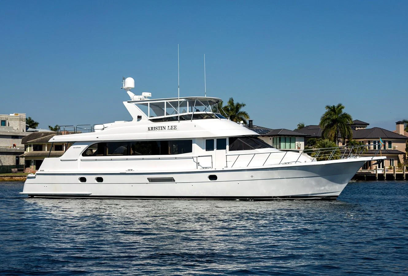 A sleek white yacht is anchored near a waterfront residential area under a clear blue sky. aboard KRISTIN LEE Yacht for Sale