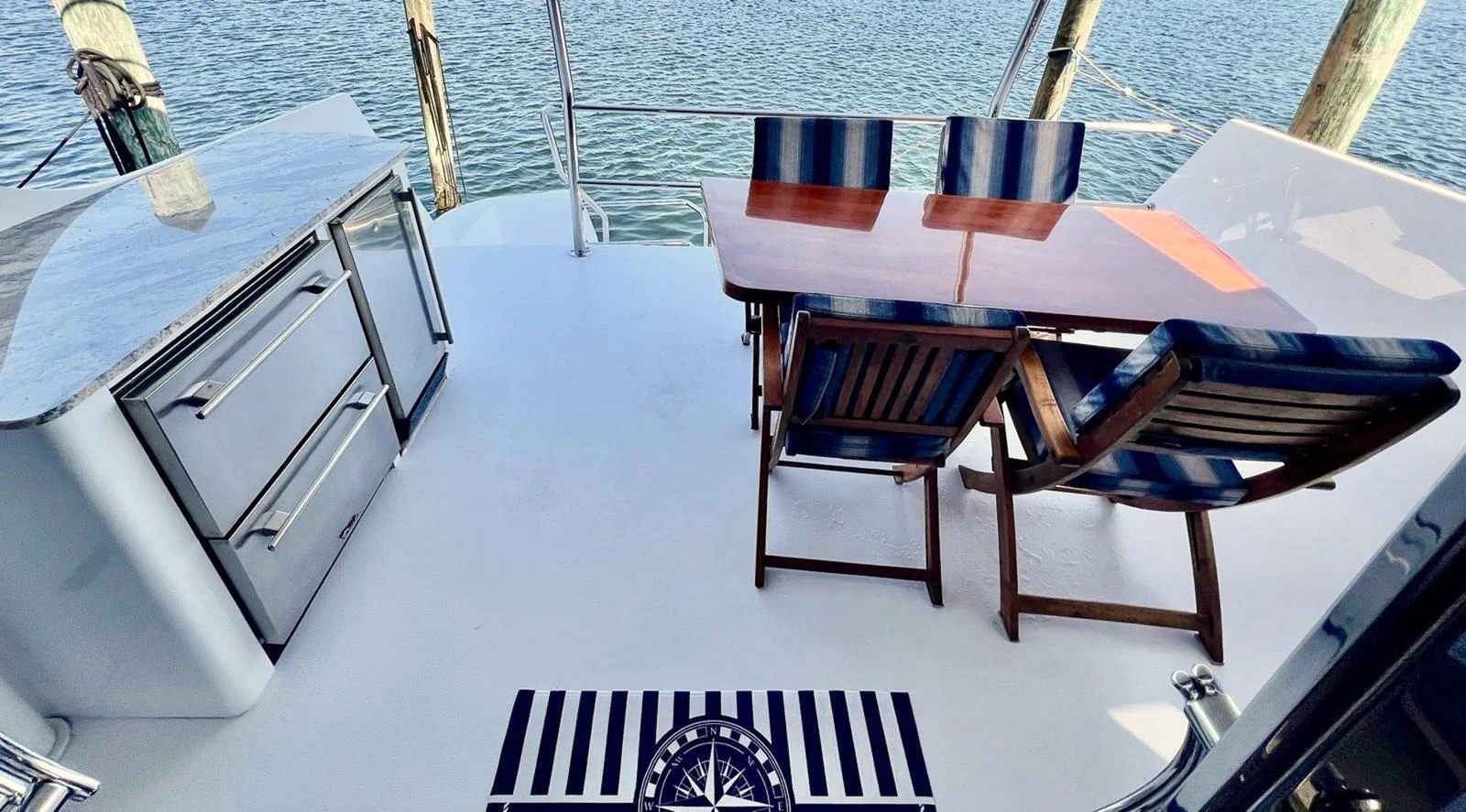The aft deck features a stylish dining area with a wooden table and striped chairs, complemented by a sleek outdoor kitchen setup. aboard KRISTIN LEE Yacht for Sale