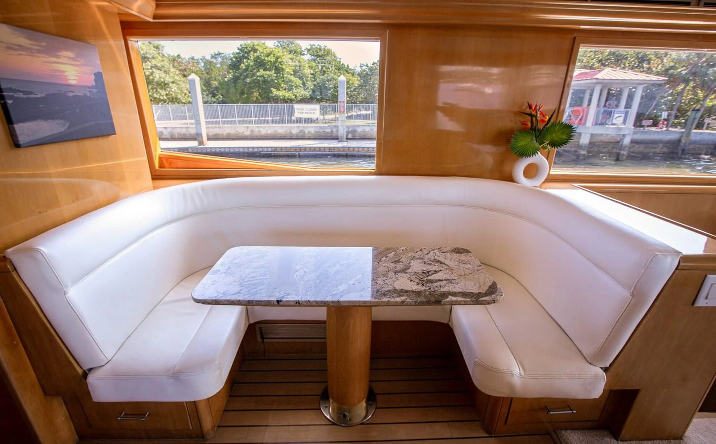 The yacht's interior dining area features a cozy, white upholstered seating arrangement with a marble-topped table, set against large windows offering scenic views. aboard KRISTIN LEE Yacht for Sale