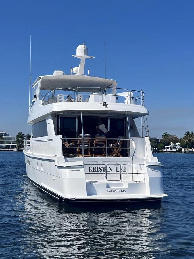 A luxurious yacht is seen from the rear, cruising on calm waters under a clear blue sky. aboard KRISTIN LEE Yacht for Sale