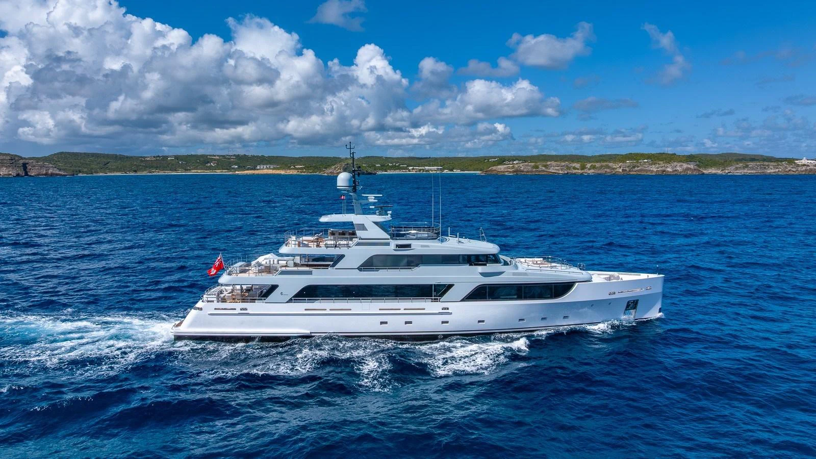 A sleek and modern yacht glides through the vibrant blue waters under a partly cloudy sky. aboard GIOIA Yacht for Sale
