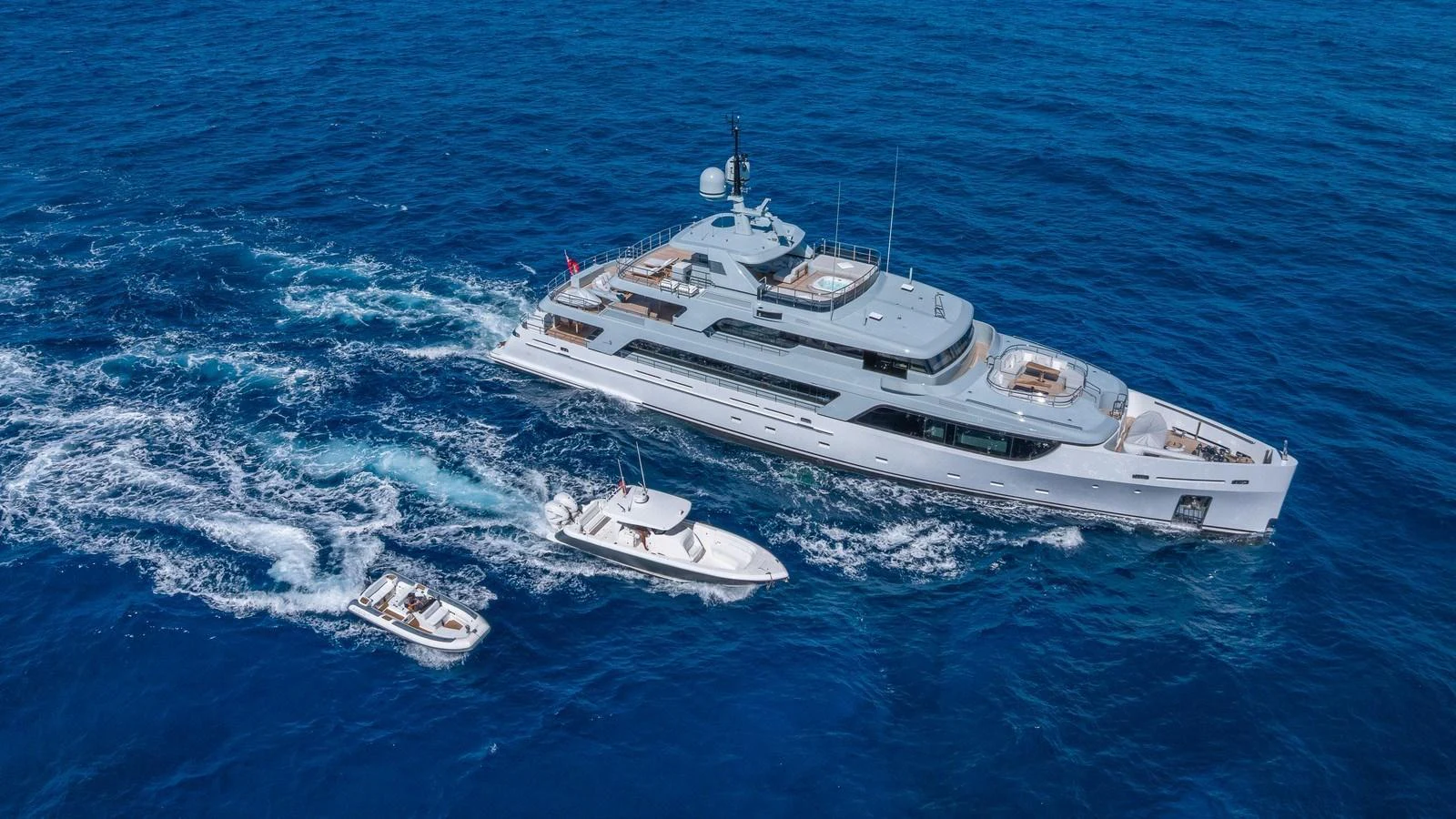 A sleek yacht cruises through the open sea accompanied by two smaller boats. aboard GIOIA Yacht for Sale