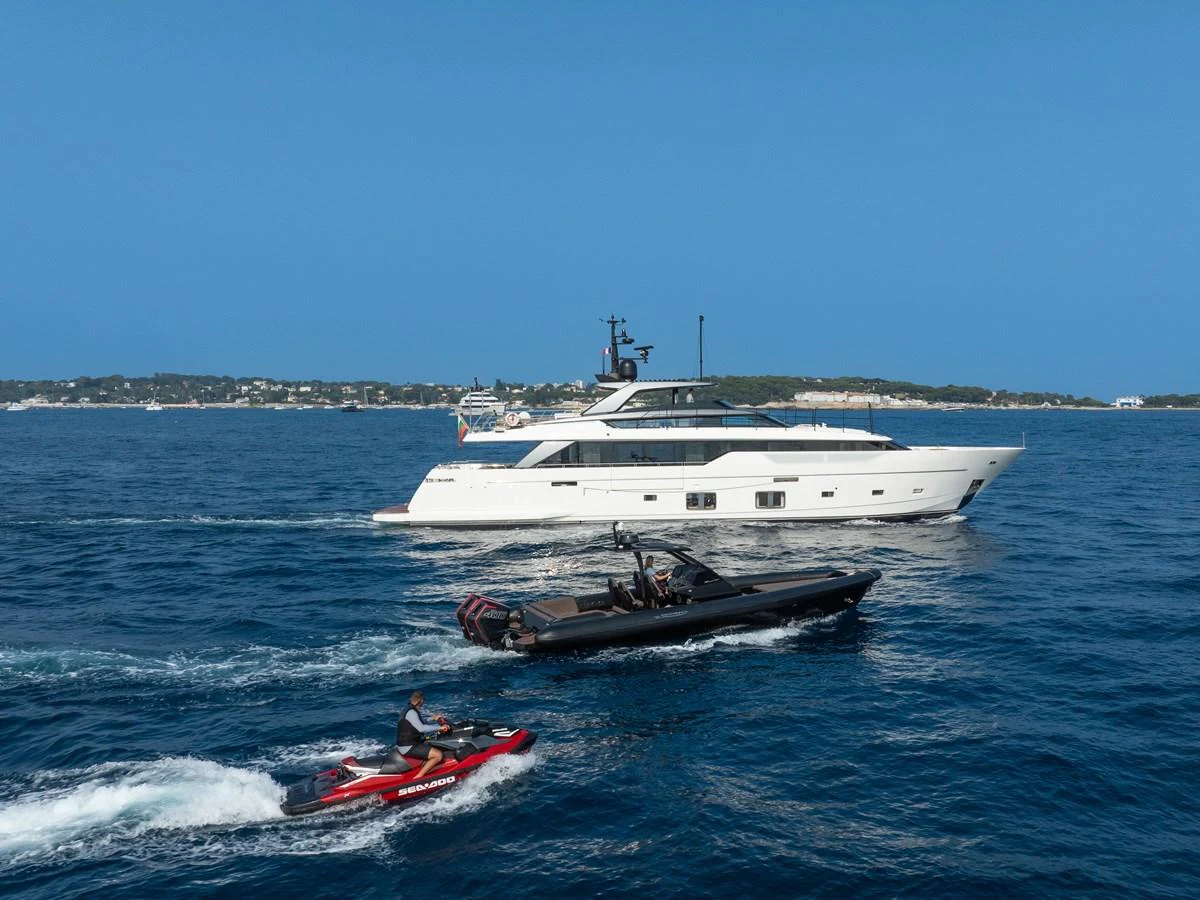 A sleek, modern yacht cruises through clear blue waters, accompanied by a tender and a jet ski. aboard NANGARA Yacht for Sale