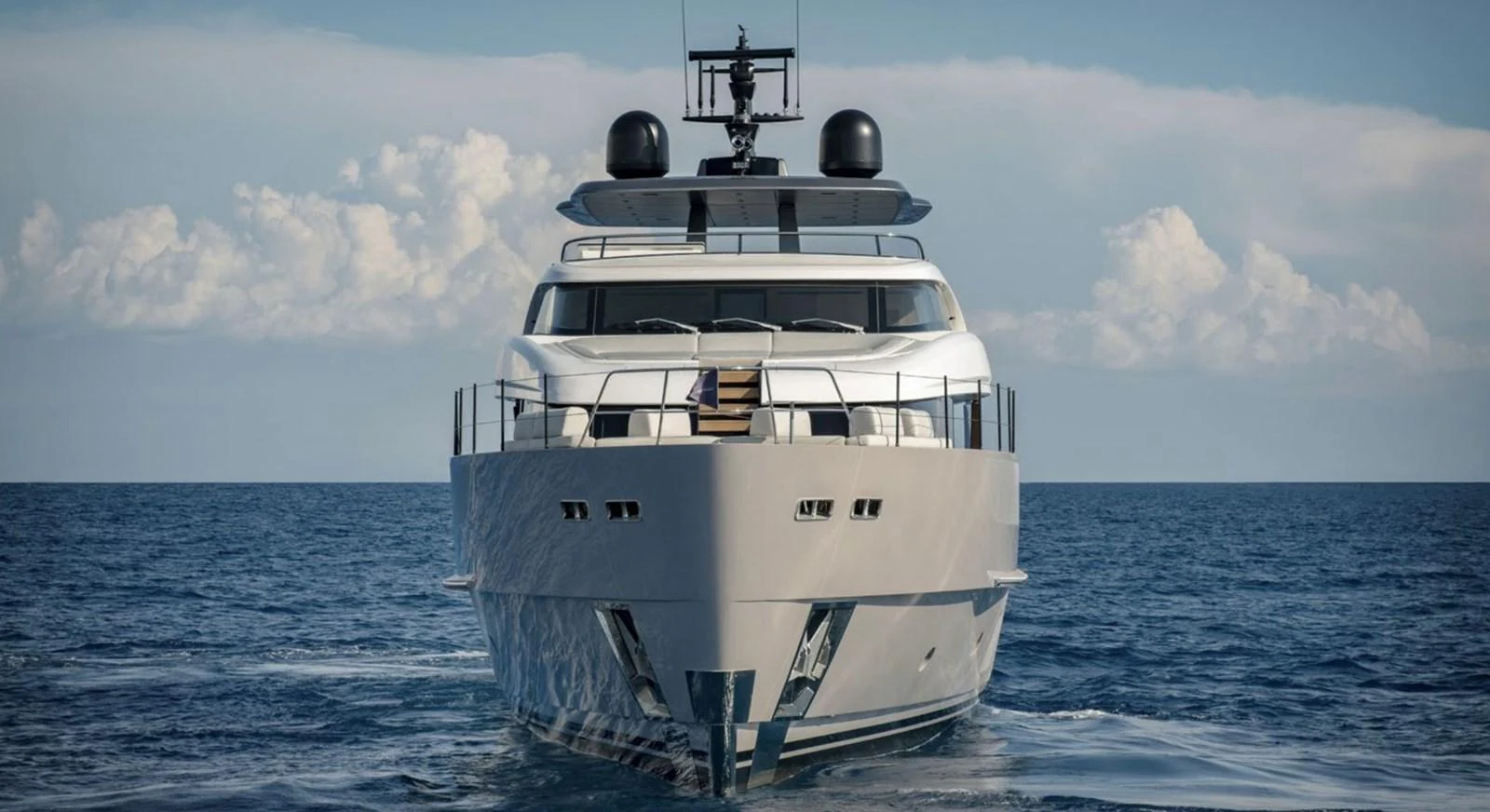 A sleek and modern yacht is seen head-on, cruising on calm waters under a partly cloudy sky. aboard SD90 Yacht for Sale