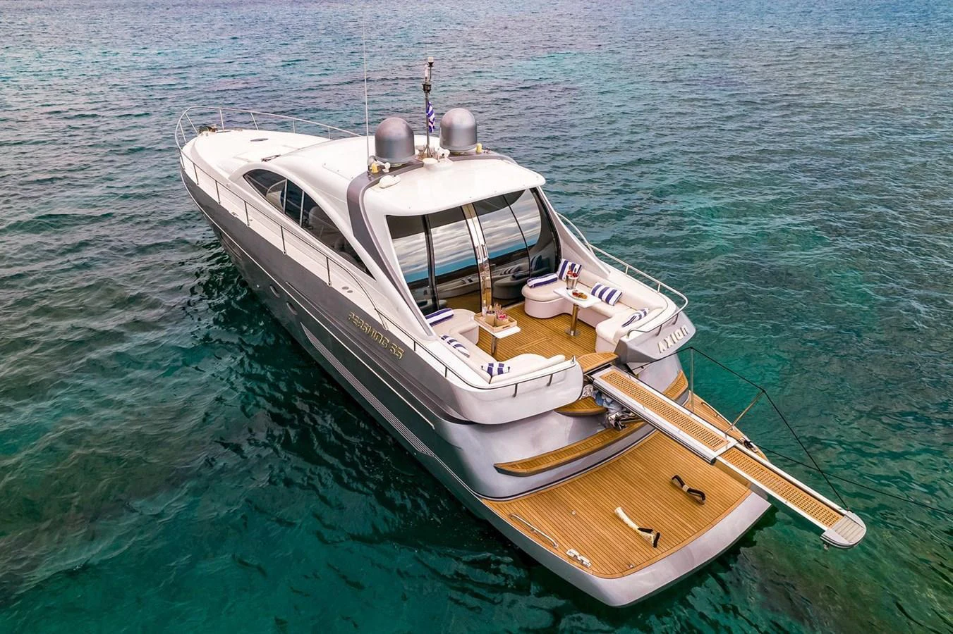 A sleek yacht with a spacious aft deck featuring comfortable seating and a swim platform, cruising on clear blue waters. aboard AXION Yacht for Sale