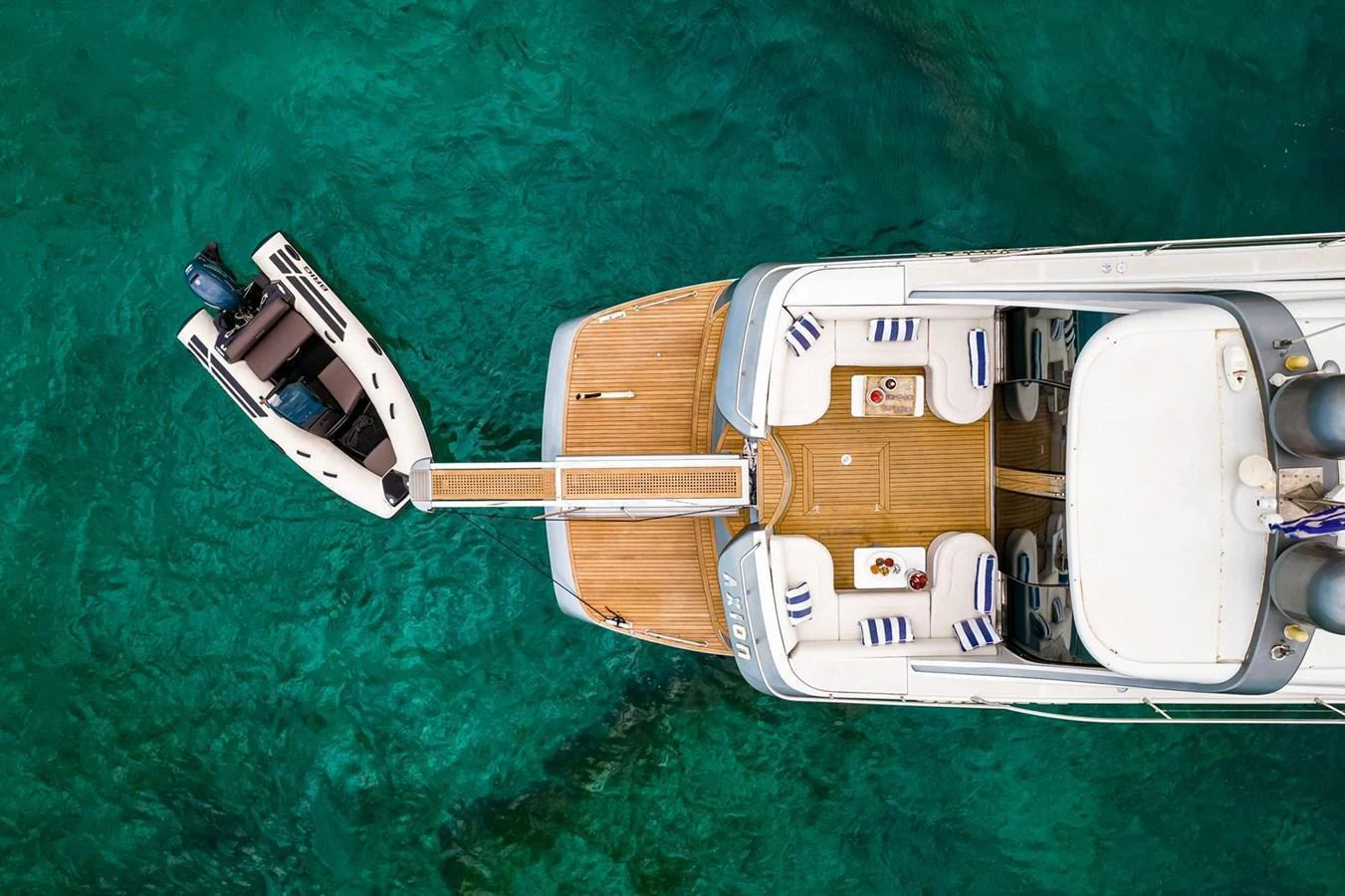 The yacht's aft deck features a spacious lounging area with a tender docked alongside in crystal-clear waters. aboard AXION Yacht for Sale