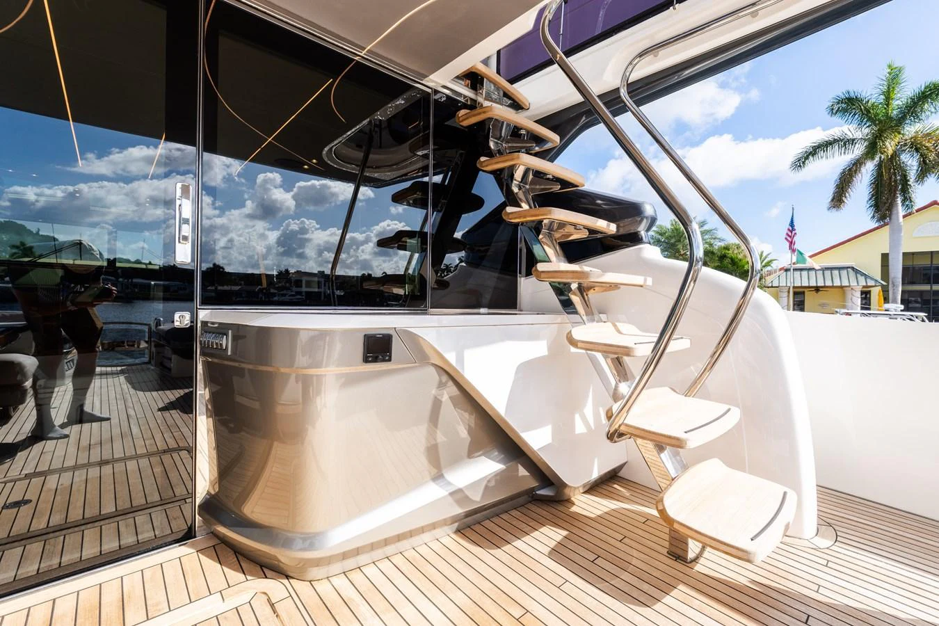 The aft deck features a sleek staircase leading to the upper deck, with polished wood flooring and modern design elements. aboard NAUTI NATALIE Yacht for Sale