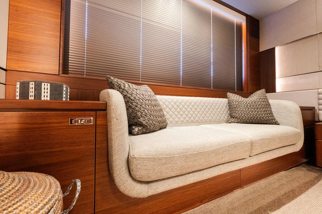 The yacht's salon features a comfortable sofa with elegant cushions, set against a backdrop of warm wood paneling and modern blinds. aboard NAUTI NATALIE Yacht for Sale