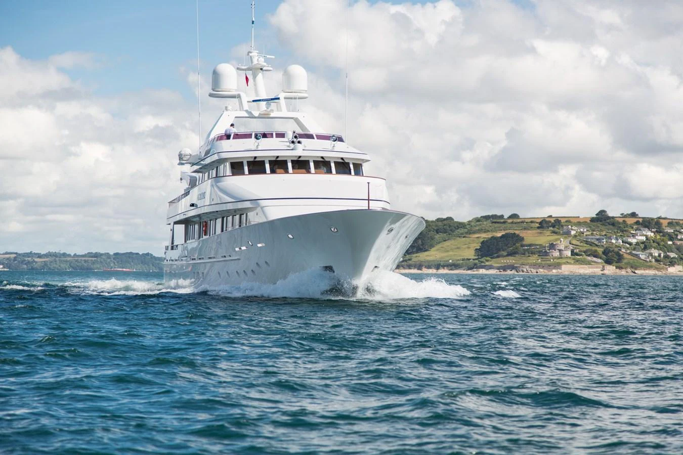 A luxurious yacht cruises through open waters with a scenic coastline in the background. aboard CONSTANCE Yacht for Sale