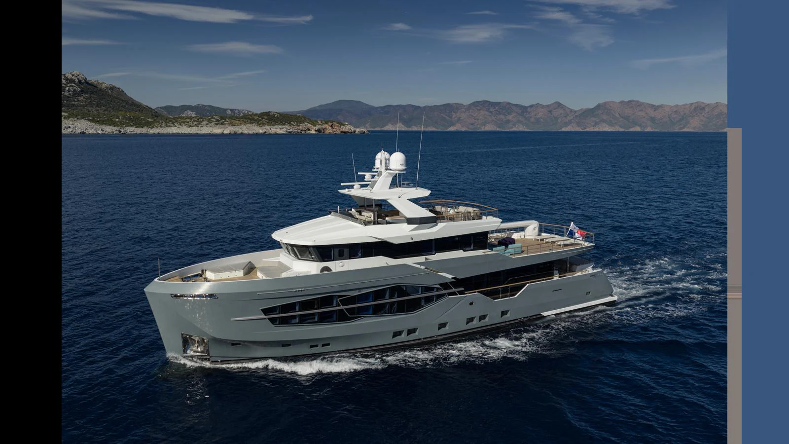 A sleek and modern yacht cruises through clear blue waters with a scenic coastline in the background. aboard Q.M Yacht for Sale