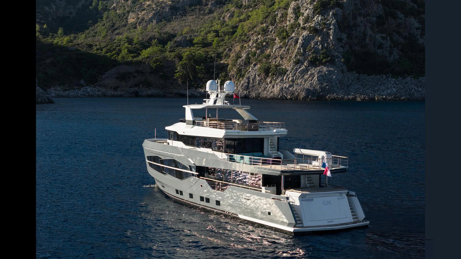 A luxurious yacht cruises through serene waters with a stunning rocky coastline in the background. aboard Q.M Yacht for Sale