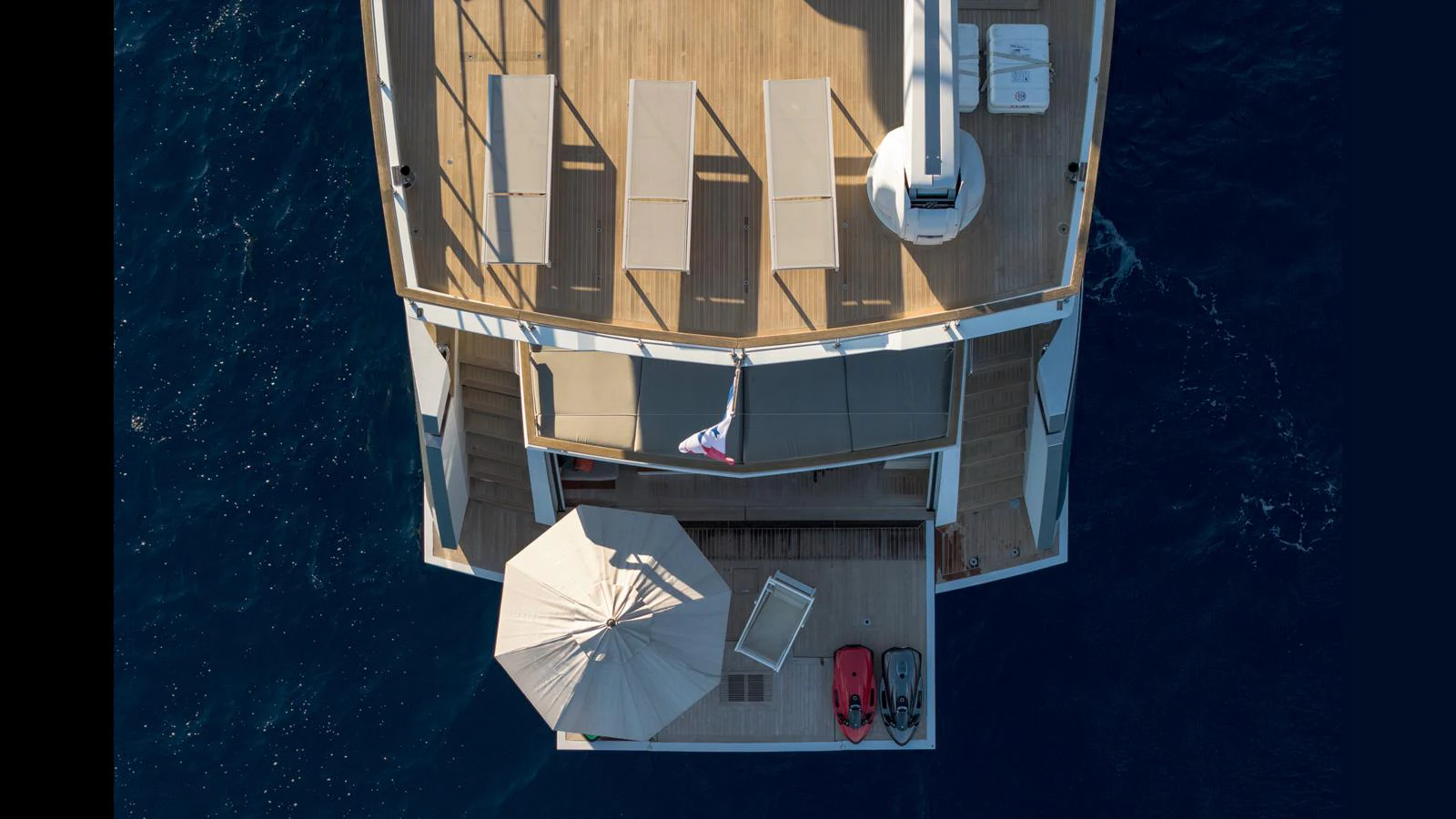 Aerial view of the yacht's aft deck featuring sun loungers, an umbrella, and water toys. aboard Q.M Yacht for Sale